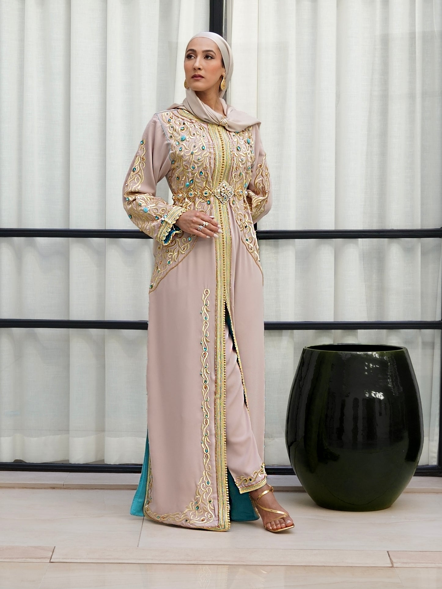 Caftan marocain Aaliya beige, broderies or et perles turquoise et fuchsia. Porté debout, il dévoile un ensemble pantalon moderne et une doublure contrastée. Tenue artisanale de luxe signée Beldyness.