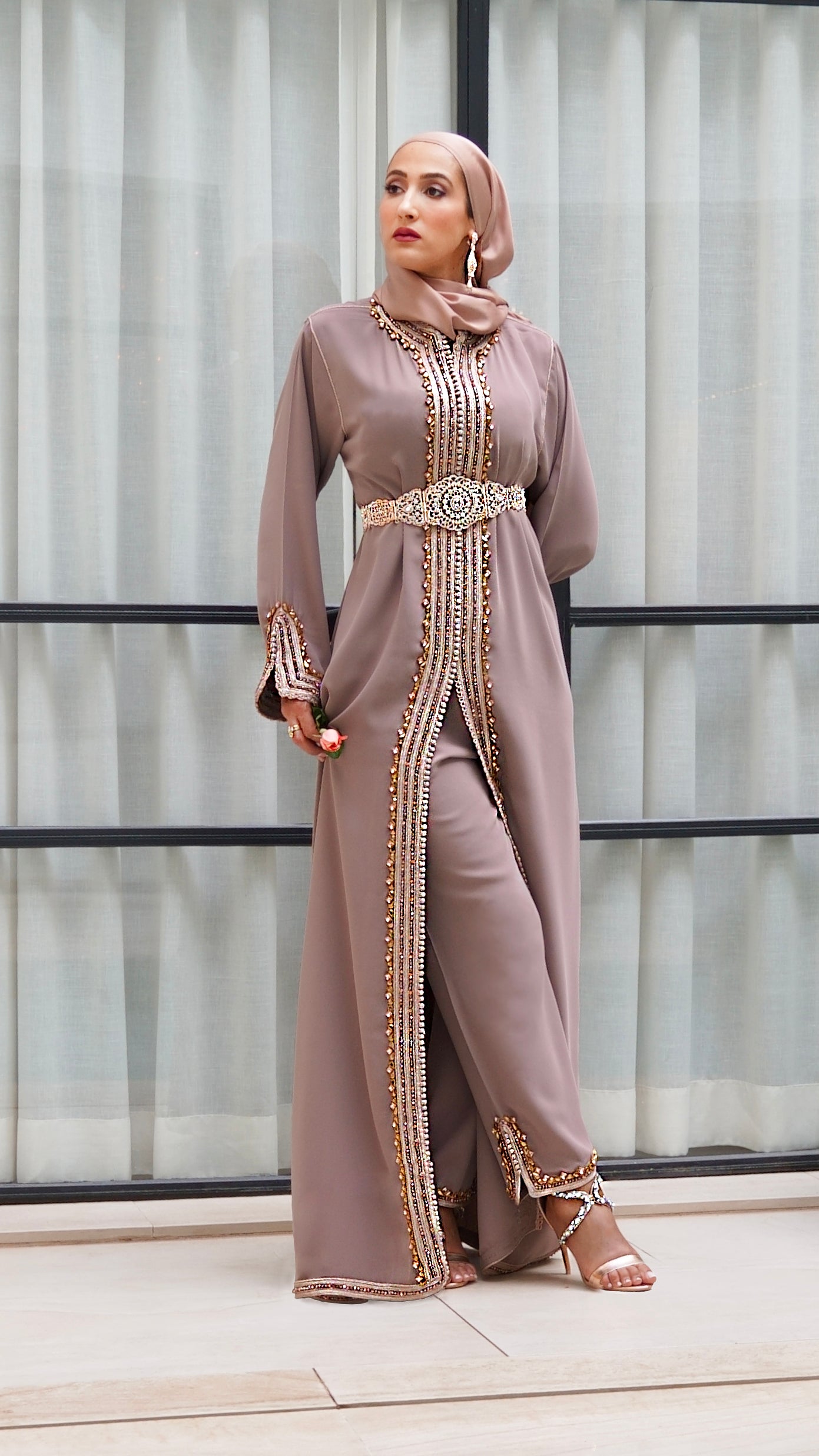 Vue en pied du caftan Jawhara taupe porté debout. Ensemble fluide composé d'une robe ceinturée et d'un pantalon opaque, offrant une silhouette majestueuse et 100% mastour.