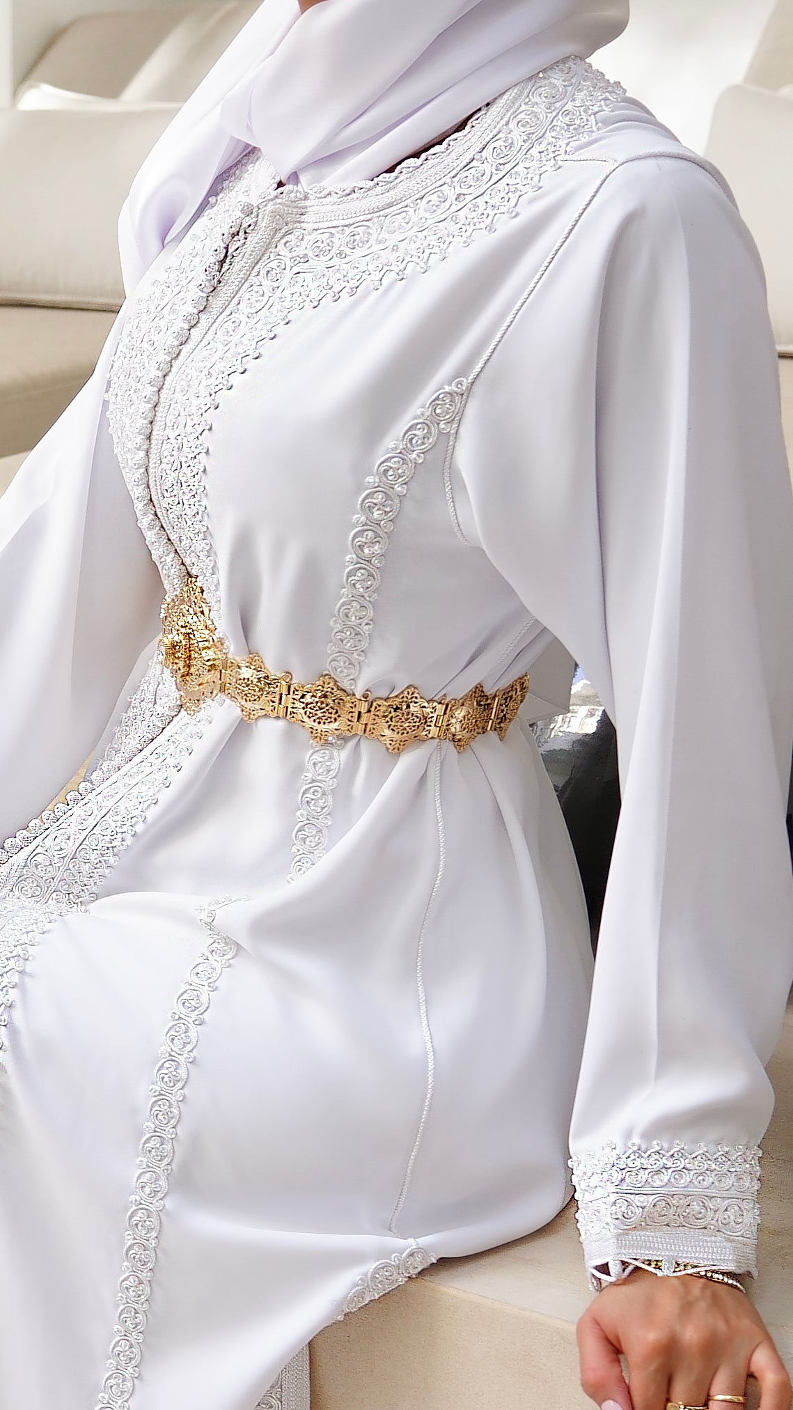 Gros plan sur les finitions Haute Facture du caftan Rawiya : broderies blanches ton sur ton minutieuses et ceinture dorée raffinée. L'art du détail par Beldyness.