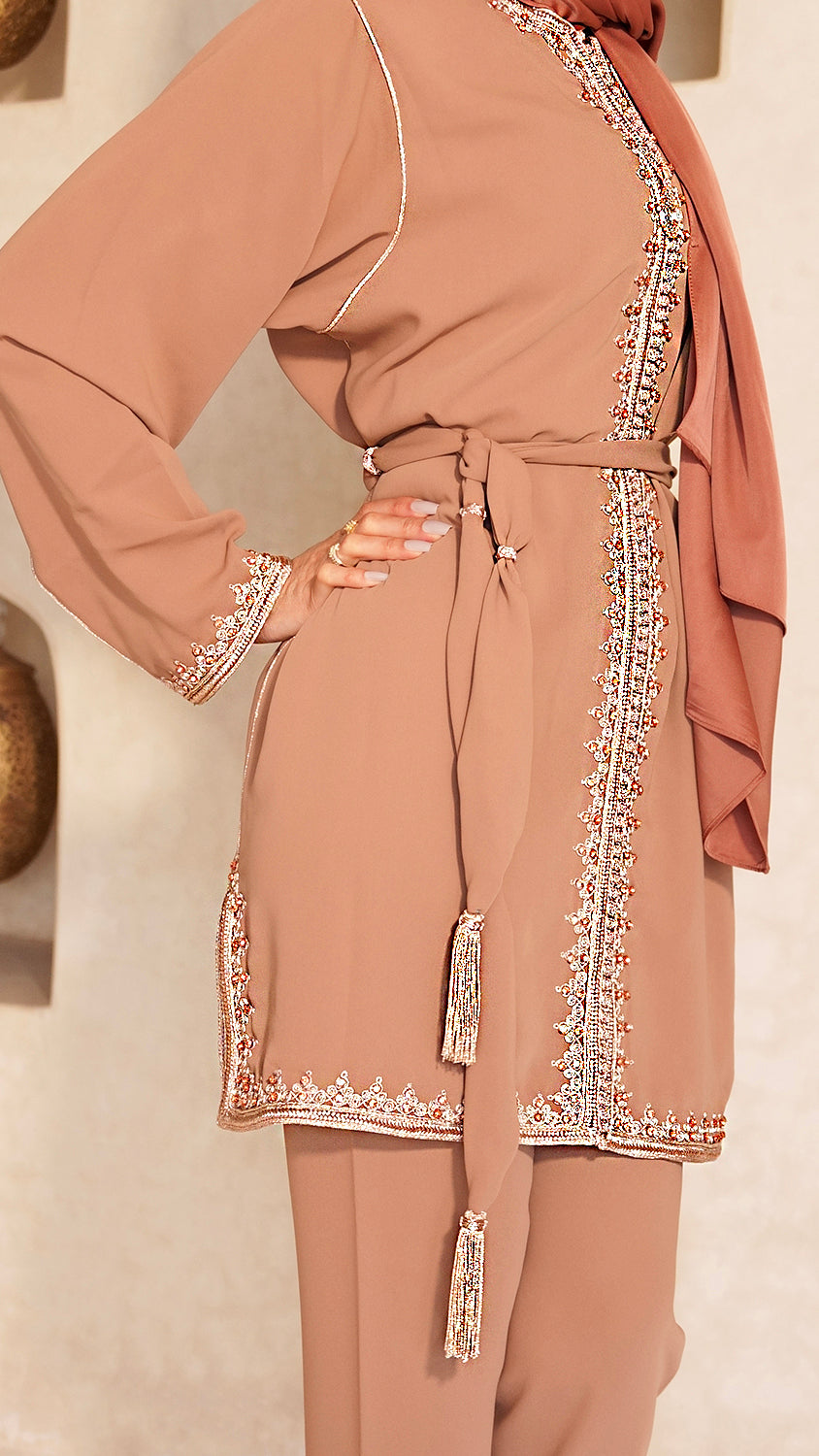Gros plan sur les finitions artisanales du Jabador Johar terracotta. Détail de la ceinture fine à pompons, de la sfifa bronze et des perles le long de la tunique et sur les manches. Travail de Haute Facture.