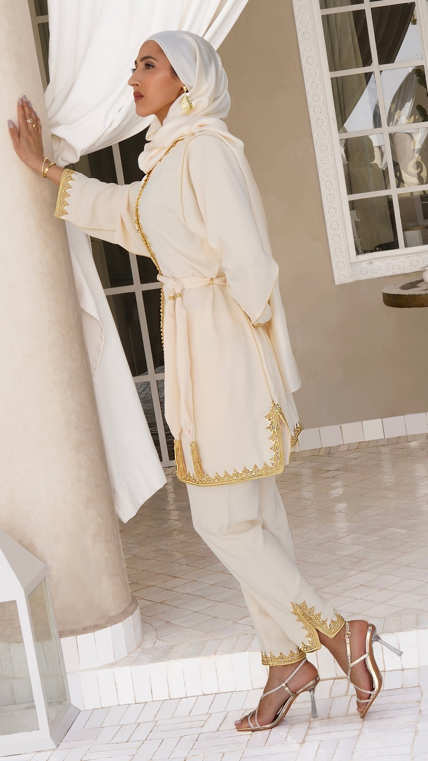 Vue d'ensemble du Jabador Johar beige crème porté debout. Un ensemble marocain 2 pièces fluide pour femme, composé d'une tunique ceinturée et d'un pantalon assorti avec broderies maalem dorées. Allure élégante et Modest Fashion par Beldyness.