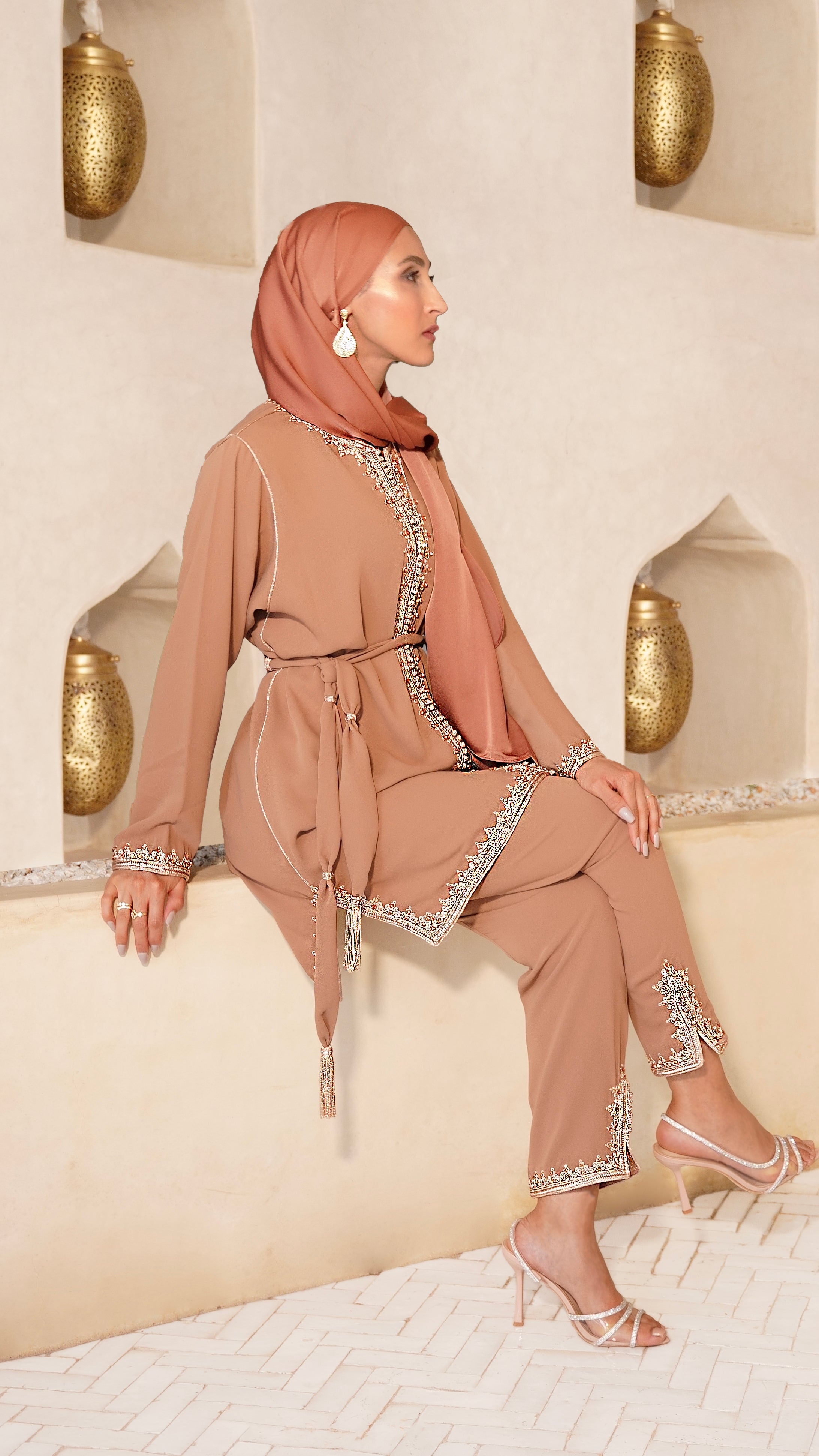 Femme élégante assise portant le Jabador Johar de couleur terracotta. Un ensemble marocain haut de gamme composé d'une tunique aux broderies bronze et perles ton sur ton et d'un pantalon assorti. Création Modest Fashion signée Beldyness.