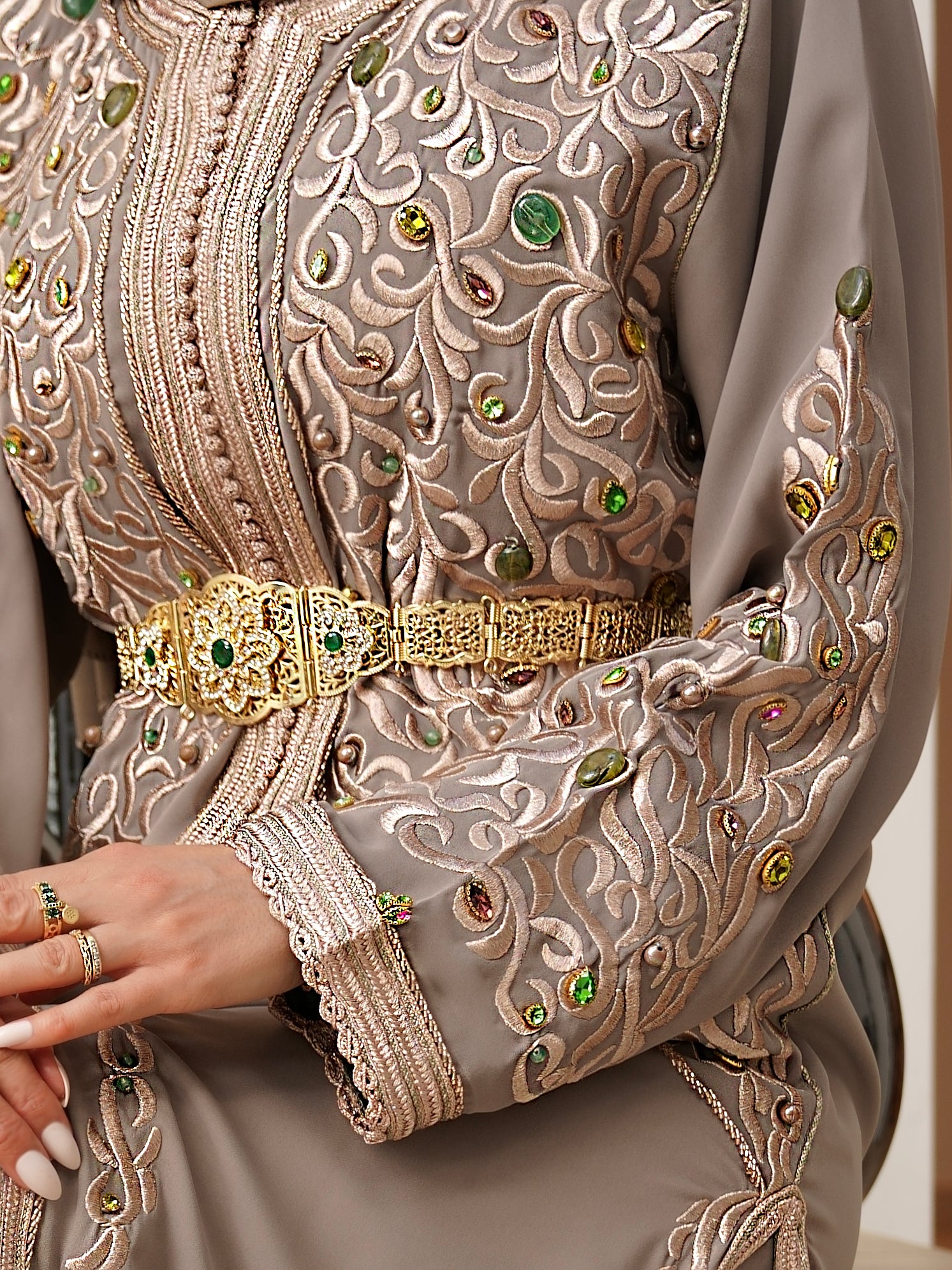 Gros plan sur les broderies artisanales bronze et les pierres vert émeraude du Caftan Aaliya kaki. Zoom sur la ceinture et le travail de finition de broderie et perles fuchsia, signature Beldyness